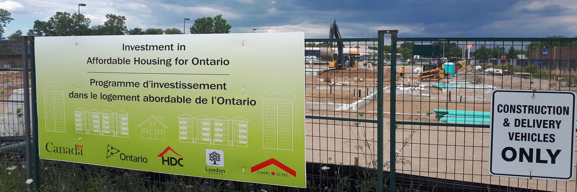 Sign at 440 Clarke Road in London Ontario listing funding partners. The sign on the site states: Investment in Affordable Housing in Ontario. Logos for the following valued funding partners are displayed: Government of Canada; Province of Ontario; Housing Development Corporation, London; the City of London; and Canada Mortgage and Housing Corporation.